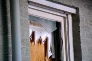 A dilapitdated property showing a broken boarded up window.